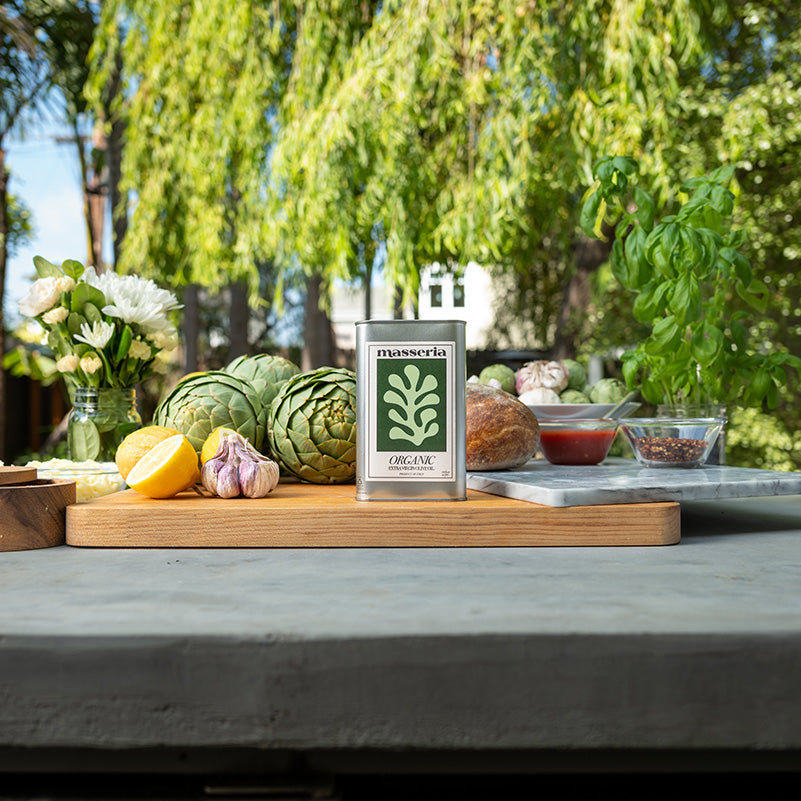 Table with fresh produce and a bottle of olive oil in an outdoor setting